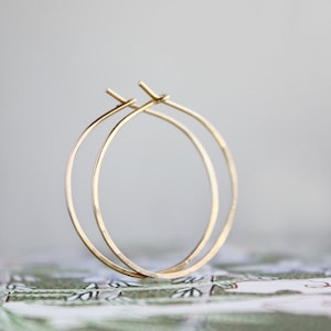 May include: A pair of gold hoop earrings. The hoops are thin and delicate, and they are made of a smooth metal.