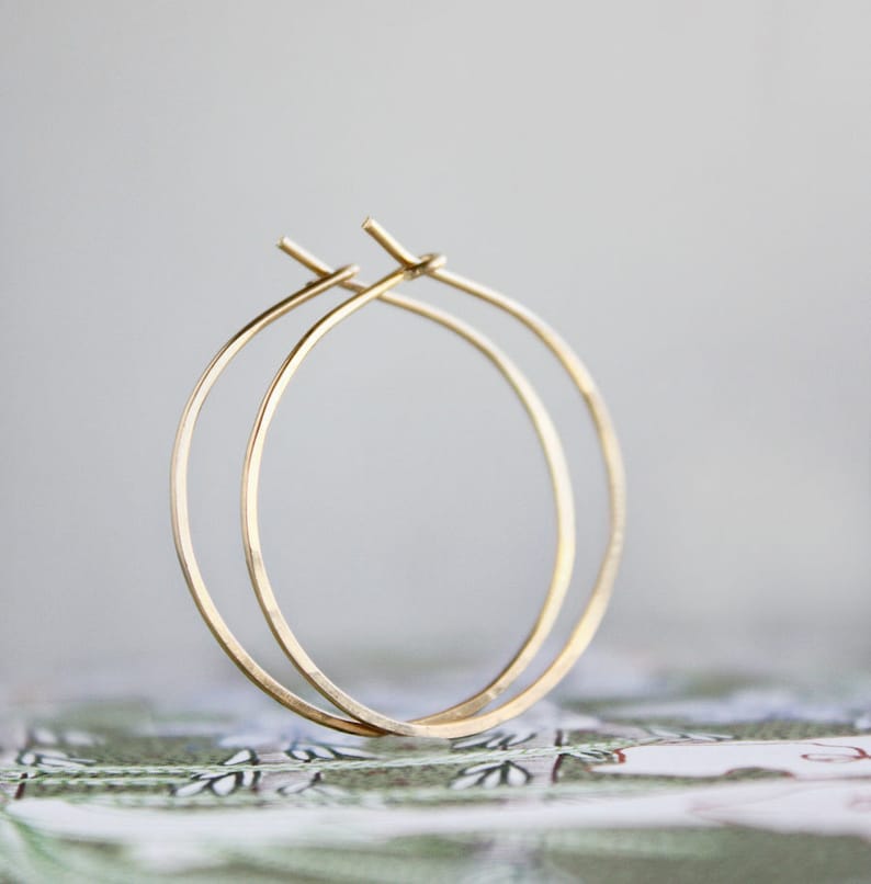 May include: A pair of gold hoop earrings. The hoops are thin and delicate, and they are made of a smooth metal.
