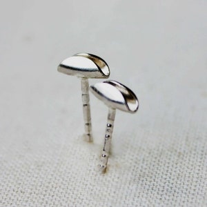 May include: A pair of silver stud earrings with a curved, half-circle shape. The earrings are simple and minimalist.