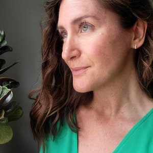 May include: A woman with long brown hair wearing a green v-neck top. She is looking to the right of the frame.