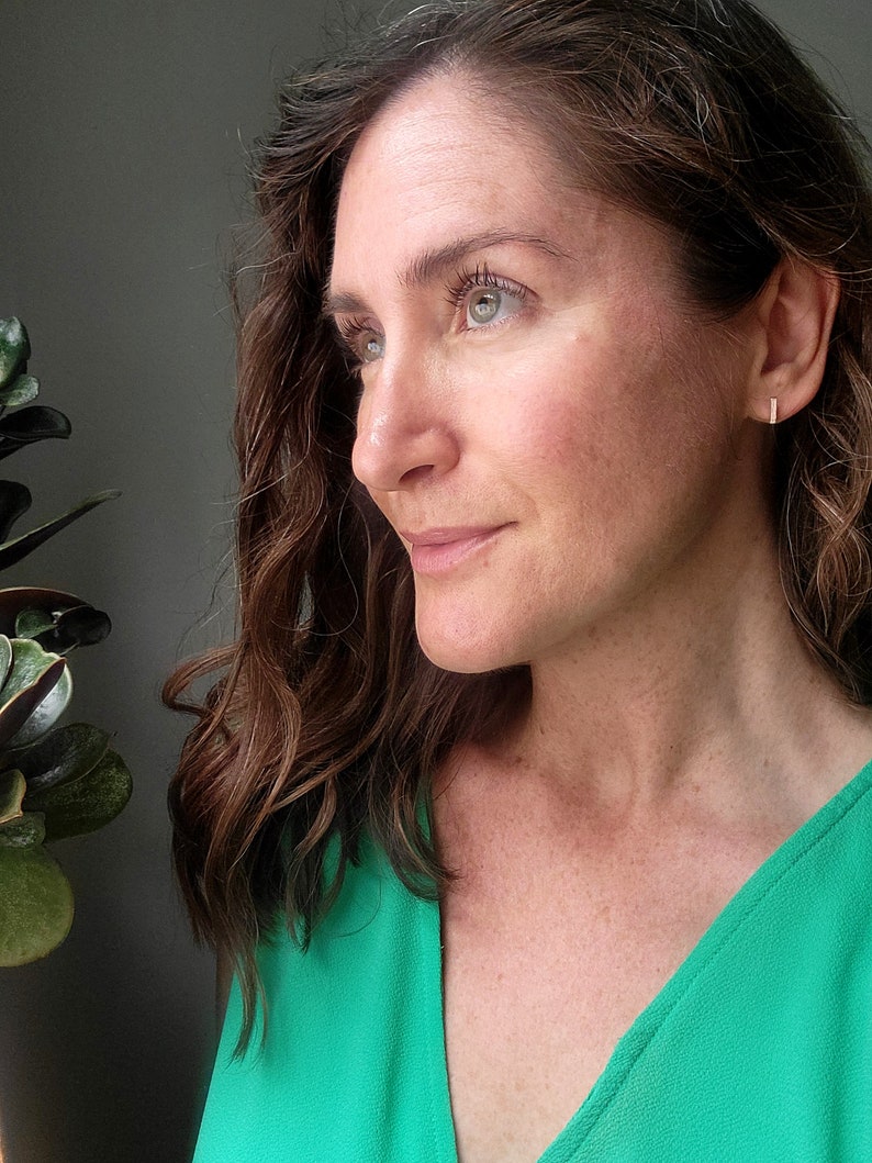 May include: A woman with long brown hair wearing a green v-neck top. She is looking to the right of the frame.