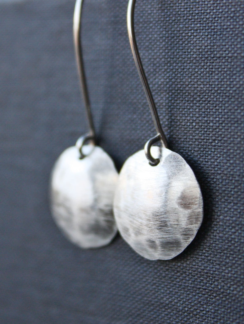 May include: A pair of silver earrings with hammered round disc pendants hanging from silver hooks.