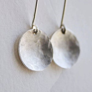 May include: A pair of silver earrings with a hammered, circular design. The earrings are simple and elegant.
