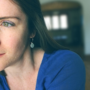 May include: A woman with long dark hair wearing a blue shirt and a silver earring.