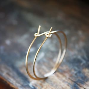 May include: A pair of gold hoop earrings with a simple, minimalist design. The hoops are thin and delicate, and they have a smooth, polished finish.