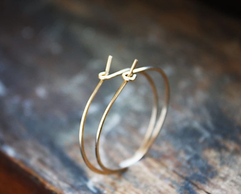May include: A pair of gold hoop earrings with a simple, minimalist design. The hoops are thin and delicate, and they have a smooth, polished finish.