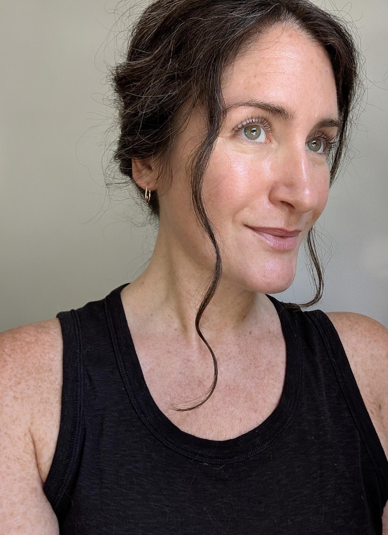 May include: A small, thin, gold-toned rectangular hoop earring worn in the earlobe. The earring features a minimalist, geometric shape with a polished metallic finish, designed as a simple, lightweight loop that secures through the ear piercing.