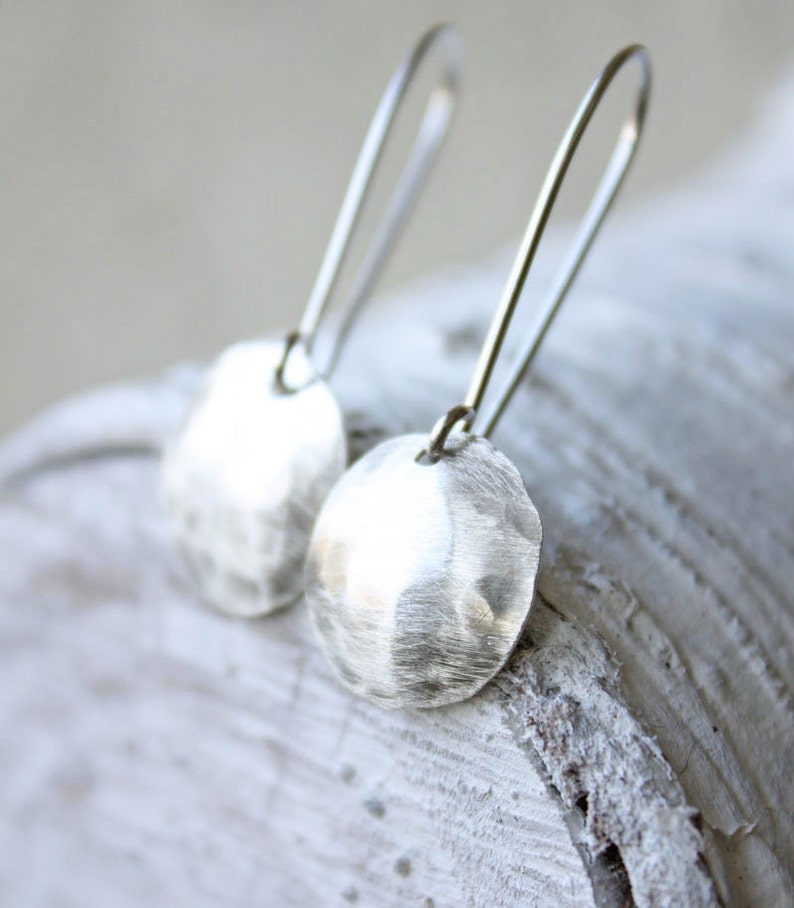 May include: A pair of silver dangle earrings with hammered round disc pendants. The earrings have a simple, minimalist design.