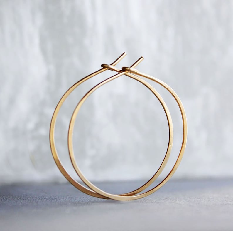May include: A pair of gold hoop earrings. The hoops are thin and delicate, and they are made of a smooth, polished metal.
