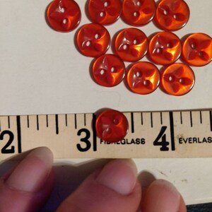 Puede incluir: Colecci&oacute;n de botones rojos transl&uacute;cidos con dise&ntilde;o de cuatro p&eacute;talos. Cada bot&oacute;n tiene dos agujeros y mide aproximadamente 2,5 cm de di&aacute;metro. Los botones est&aacute;n dispuestos sobre una superficie blanca.