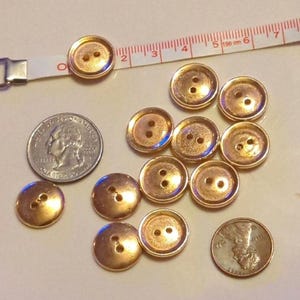 Puede incluir: Una colecci&oacute;n de 12 botones de color dorado con dos agujeros cada uno. Los botones est&aacute;n dispuestos en un c&iacute;rculo alrededor de una moneda de 25 c&eacute;ntimos y una cinta m&eacute;trica.