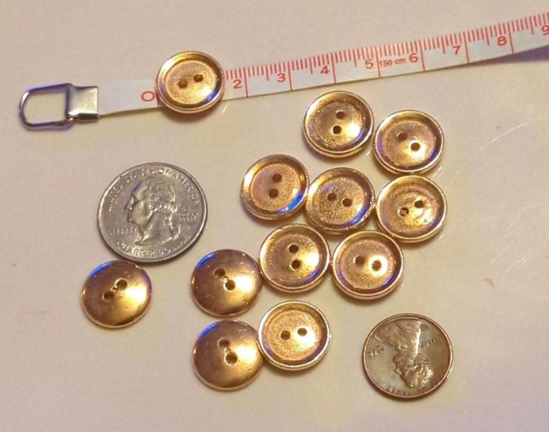 Puede incluir: Una colecci&oacute;n de 12 botones de color dorado con dos agujeros cada uno. Los botones est&aacute;n dispuestos en un c&iacute;rculo alrededor de una moneda de 25 c&eacute;ntimos y una cinta m&eacute;trica.