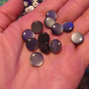 May include: A collection of round, black and grey buttons with a shiny, iridescent finish.