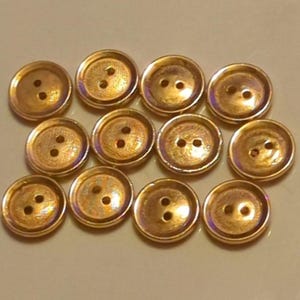 Puede incluir: Una colecci&oacute;n de 10 botones de color dorado con dos agujeros cada uno. Los botones tienen un acabado ligeramente iridiscente.