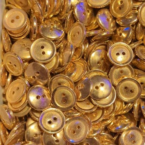 Puede incluir: Un mont&oacute;n grande de botones de color dorado con dos agujeros cada uno. Los botones son lisos y brillantes.
