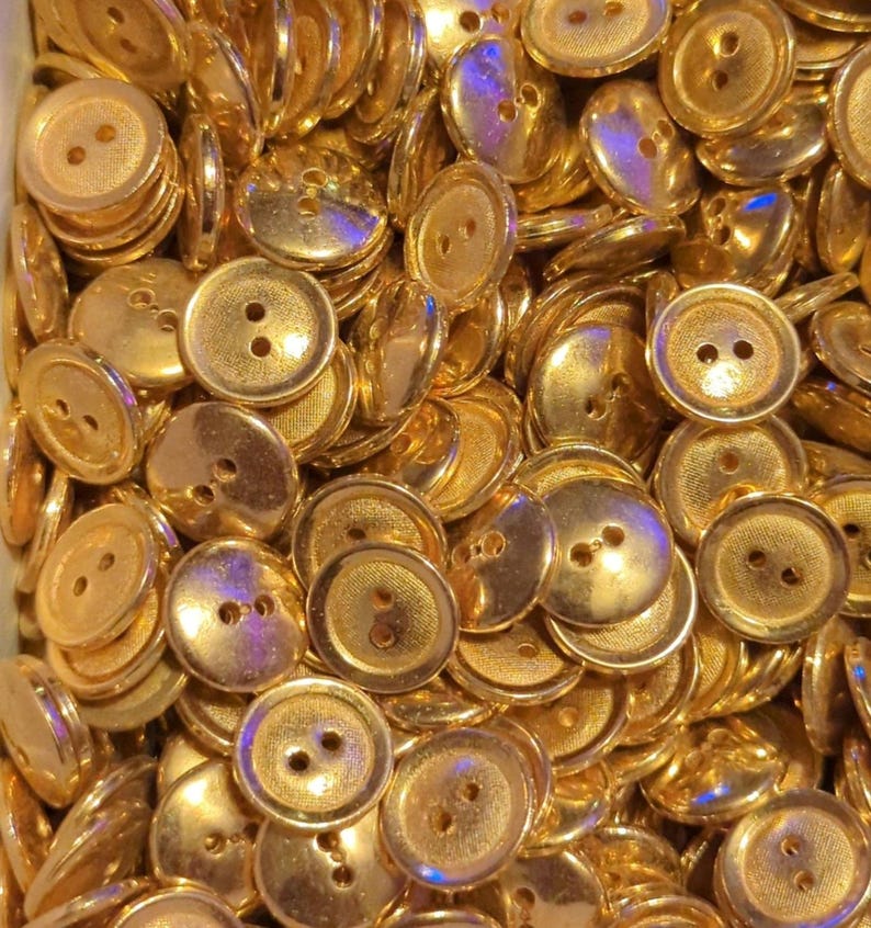 Puede incluir: Un mont&oacute;n grande de botones de color dorado con dos agujeros cada uno. Los botones son lisos y brillantes.