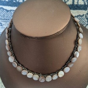 Puede incluir: Un collar de cadena plateada con una fila de cuentas de color marrón claro y blanco con forma de concha.
