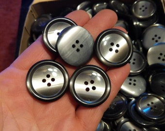 May include: A large quantity of black and silver buttons with four holes each. The buttons are arranged in a box and are being held in a hand.