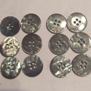 May include: Twelve round, iridescent, mother-of-pearl buttons with four holes each. The buttons are a dark gray color with a slight green hue.