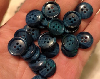May include: A collection of blue plastic buttons with four holes each. The buttons have a marbled pattern and are arranged in a pile.