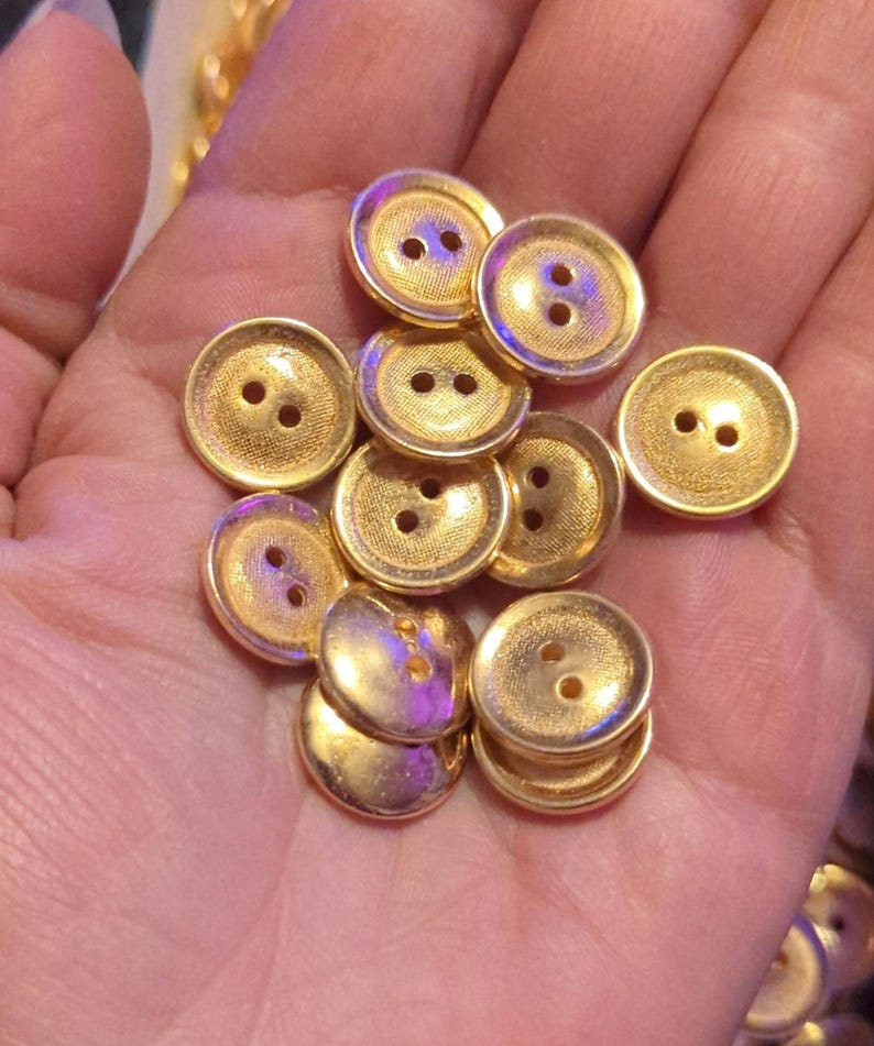 Puede incluir: Un mont&oacute;n de botones de color dorado con dos agujeros cada uno. Los botones son redondos y tienen una superficie ligeramente texturizada.