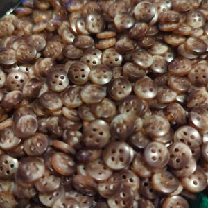 May include: A large pile of brown and white four-hole buttons. The buttons are made of a smooth, shiny material.