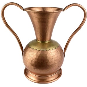 May include: A hammered copper vase with two handles and a brass rim. The vase has a round body and a flared top.