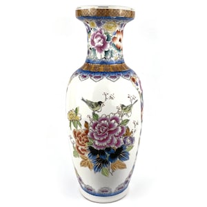 May include: A white ceramic vase with a flared top and a wide base. The vase is decorated with colourful floral and bird motifs. The flowers are in shades of pink, purple, orange, and blue. The birds are green and yellow. The vase has a blue and gold rim.
