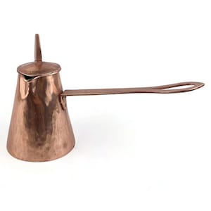 May include: A copper-coloured, hammered metal coffee pot with a long, flat handle and a small, pointed lid. The pot has a conical shape and a spout for pouring. The handle has a loop at the end for hanging.