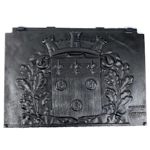 Peut inclure: Insert de cheminée rectangulaire en fonte noire avec un motif en relief détaillé. Le motif présente des armoiries avec une couronne, des fleurs de lys et trois emblèmes circulaires, encadrés de feuilles de chêne. Le texte "CHEMINEES PHILIPPE" est visible.