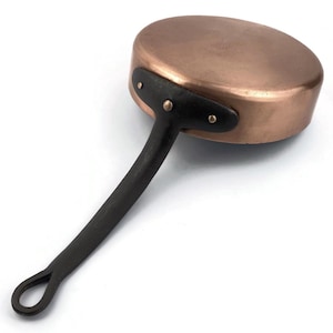 Peut inclure: Une casserole en cuivre avec une poignée sombre. La casserole a une forme arrondie et une poignée noire fixée avec des rivets. La poignée est longue et se termine par une boucle. Le cuivre a une surface brillante et réfléchissante.