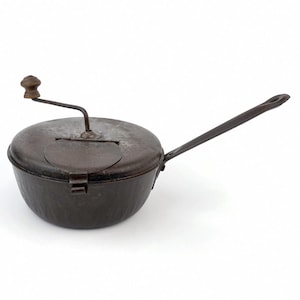 May include: Antique metal popcorn popper with a long handle and a wooden knob. The popper has a round body and a lid with a crank. The handle is approximately 15 inches long. The popper is a dark, aged metal color.