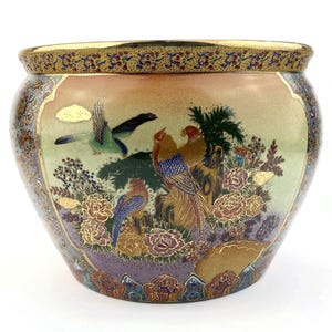 Puede incluir: Una maceta redonda de cerámica con borde dorado y una escena pintada detallada. La escena presenta pájaros coloridos, flores y follaje en tonos de azul, verde, rojo y dorado. La maceta tiene una abertura ancha y un cuerpo redondeado.