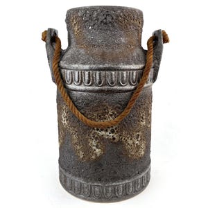 May include: A textured, cylindrical vase with a dark gray and brown color scheme. The vase features a rope handle and decorative bands around the top and bottom. The overall design has a rustic, vintage aesthetic.