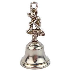 May include: Silver-toned bell with a seated fairy figurine atop. The fairy is detailed with pointed ears and a skirt-like base. The bell has a loop for hanging.