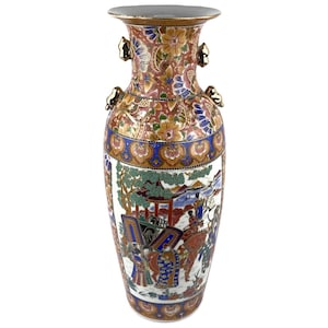 Puede incluir: Un jarrón de cerámica alto y ornamentado con boca ancha y dos asas pequeñas. El jarrón presenta un diseño detallado y colorido con motivos florales, detalles dorados y una escena que representa figuras con vestimenta tradicional. El jarrón mide unos 30 cm de alto.