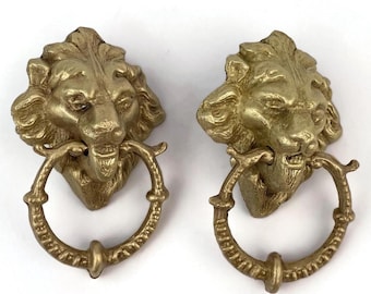 Puede incluir: Dos aldabas de puerta de latón con forma de cabeza de león. Cada aldaba presenta una cabeza de león detallada que sostiene un asa en forma de anillo. El latón tiene un acabado dorado ligeramente envejecido, lo que añade a la estética vintage. Ideal para la decoración del hogar.