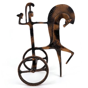 Puede incluir: Escultura de bronce de un carro tirado por un caballo. El carro tiene dos ruedas y una figura de conductor. El caballo tiene una melena detallada y está en posición de encabritado. La escultura está sobre un fondo blanco.