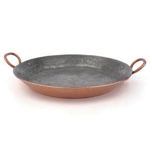 Può includere: Una padella per paella in rame e stagno con due manici. La padella è rotonda e ha una finitura martellata.