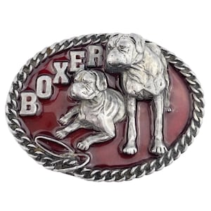 May include: Oval-shaped silver-colored belt buckle with a red background. The buckle features two Boxer dog figures and the word "BOXER" in silver letters. The border has a silver rope design.