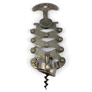 May include: Vintage metal Zig Zag corkscrew with a handle and a worm. The handle is marked "ZIG ZAG". The corkscrew has an accordion-style mechanism and a silver finish. The worm is black.