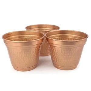 Puede incluir: Tres macetas de cobre martilladas. Las macetas son de color cobre claro y tienen una textura martillada.
