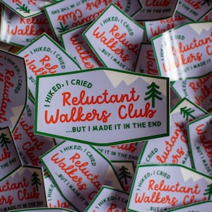 May include: A collection of stickers with the text "I Hiked, I Cried, Reluctant Walkers Club...But I Made It In The End." The stickers have a green border, orange text, and a mountain and tree graphic.