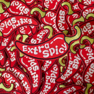 May include: A close-up of a red chili pepper patch with the text "Extra Spicy" embroidered on each pepper. The peppers are arranged in a random pattern, creating a vibrant and spicy visual.