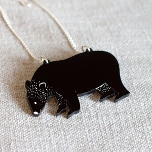 May include: A black bear silhouette pendant necklace with a silver chain. The bear is facing left and has a detailed outline.