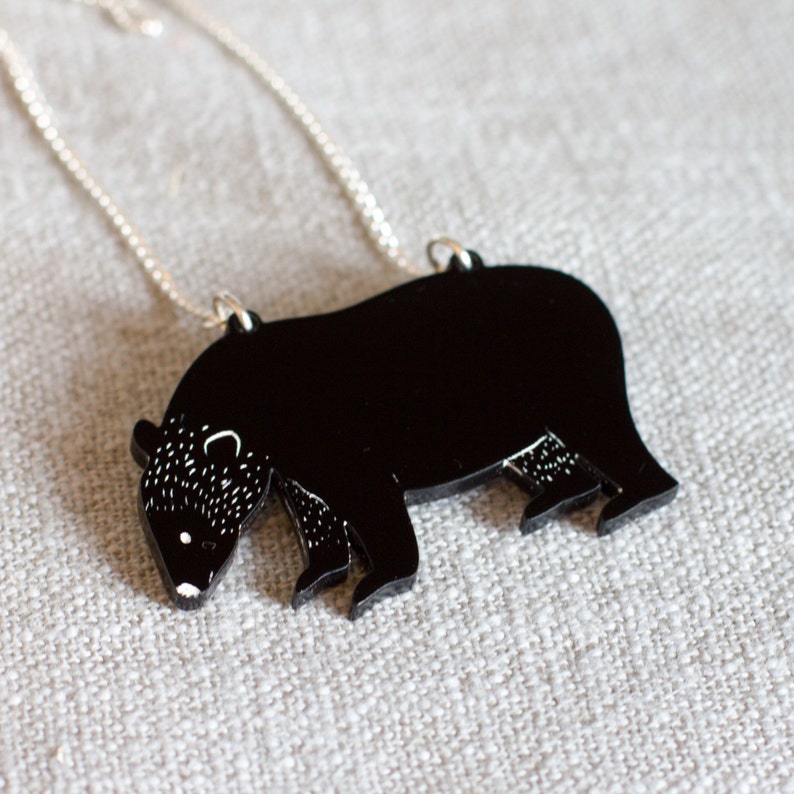 May include: A black bear silhouette pendant necklace with a silver chain. The bear is facing left and has a detailed outline.