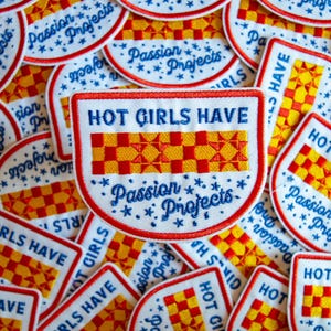May include: A collection of white, red, yellow, and blue embroidered patches. The patches have the text "HOT GIRLS HAVE" and "Passion Projects" in blue script. The patches feature a red and yellow checkered design.