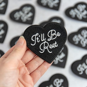 Peut inclure: Patch en forme de cœur noir avec une broderie blanche qui dit "It'll Be Reet".