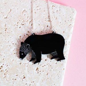 May include: A black bear silhouette pendant necklace on a silver chain. The pendant is made of acrylic and has a detailed outline of a bear.