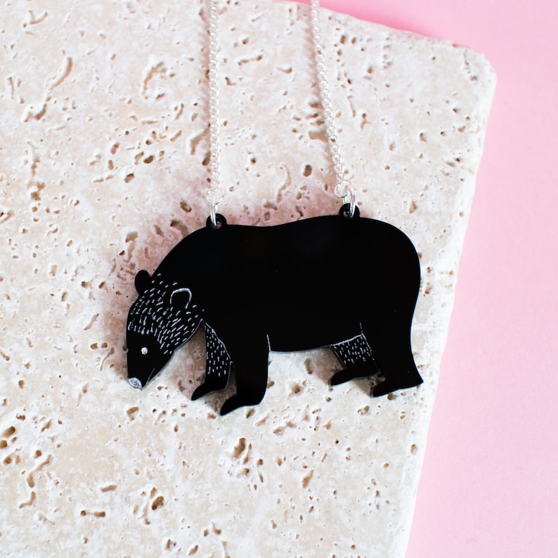 May include: A black bear silhouette pendant necklace on a silver chain. The pendant is made of acrylic and has a detailed outline of a bear.